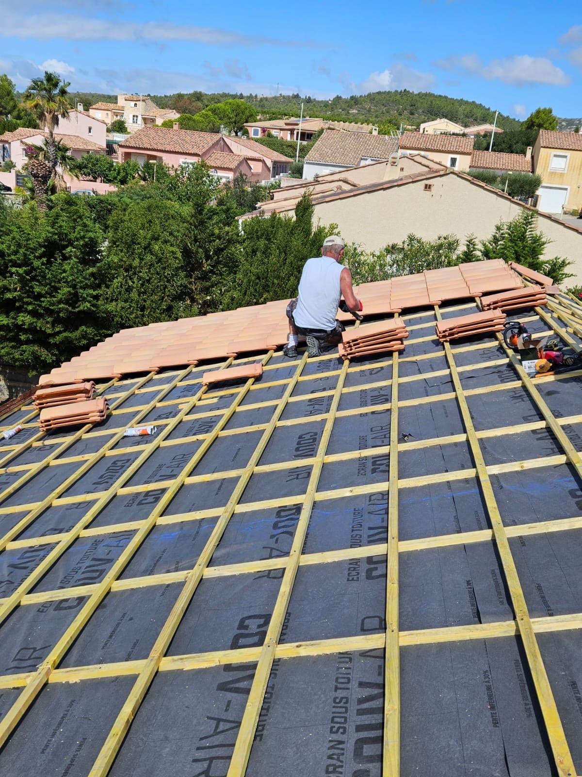 Artisan en train de poser des tuiles sur une toiture en rénovation
